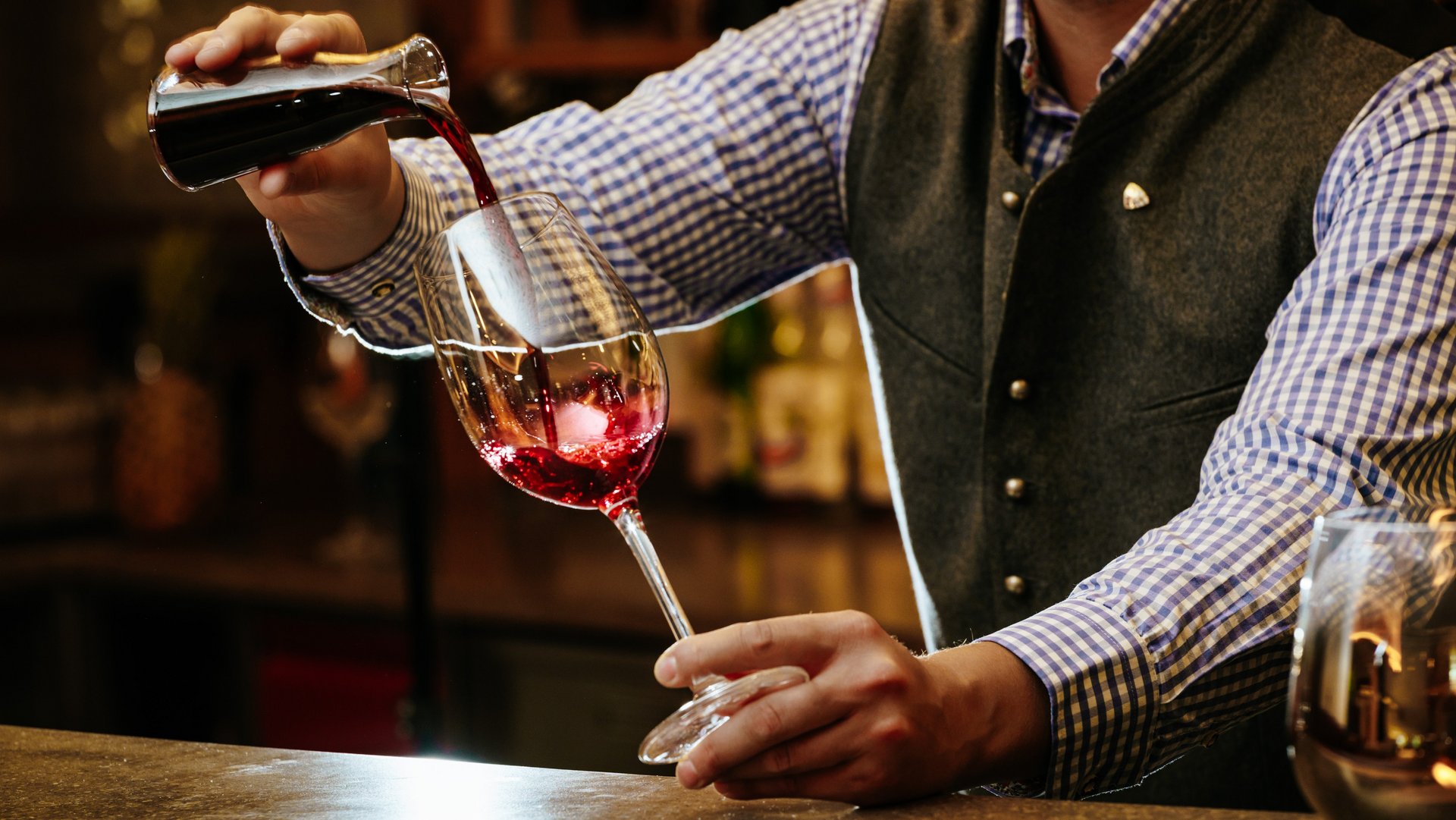 Barkeeper füllt Rotwein aus einer Karaffe in ein Weinglas am Barplatz ein und sorgt für Gastfreundschaft.