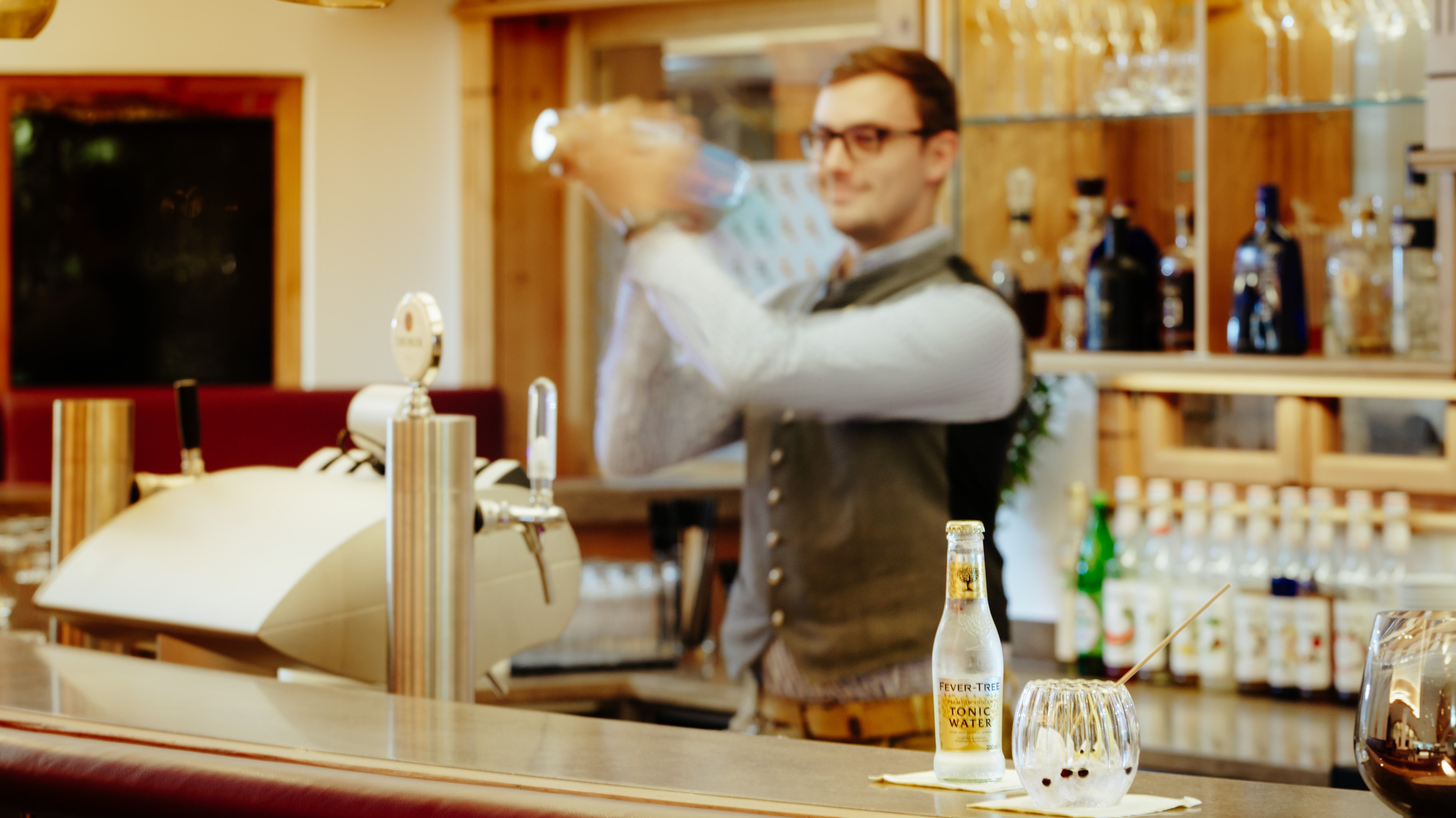 Crafting Unique Cocktails at Hirschen Hotel Bar A bartender skillfully prepares a cocktail behind the bar with a variety of drinks in view.