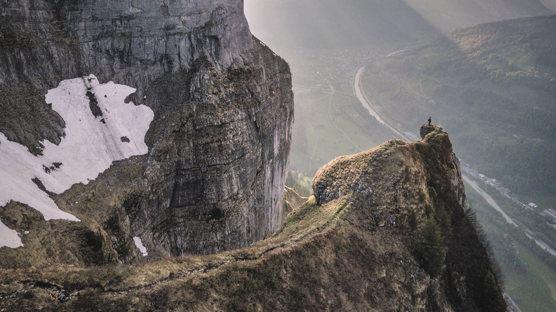 Beeindruckende Berglandschaft mit Hochgebirgen und einem darunterliegenden Tal, Sonnenstrahlen durchbrechen die Wolken