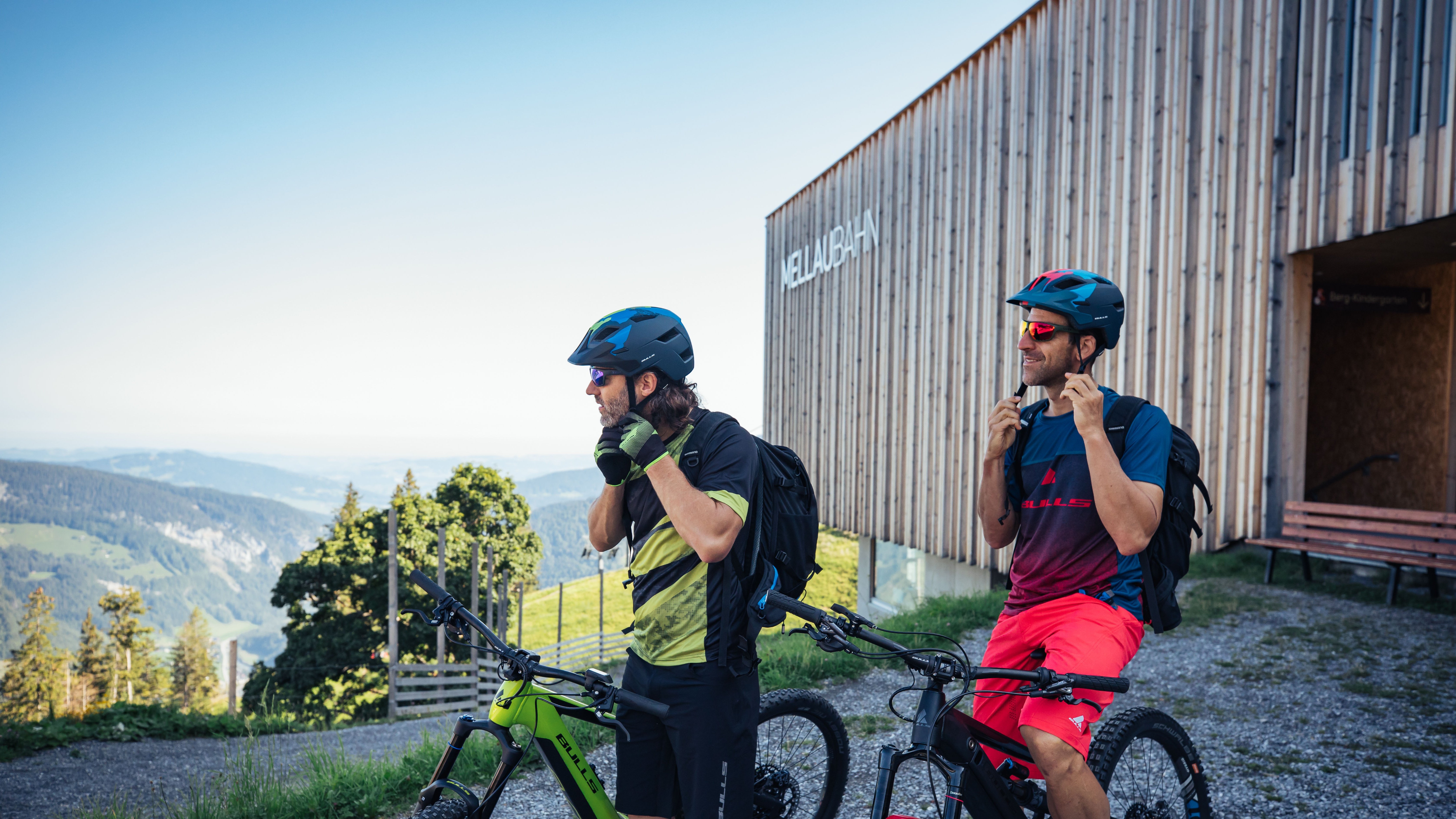 Mountainbike Abenteuer am Hirschen Wohlfühlhotel Zwei Radfahrer bereiten sich auf eine Mountainbiketour an einer Berghütte vor, umgeben von Natur.